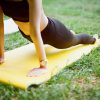 Female person doing a yoga stretch on a yellow mat outdoors, on top of grass