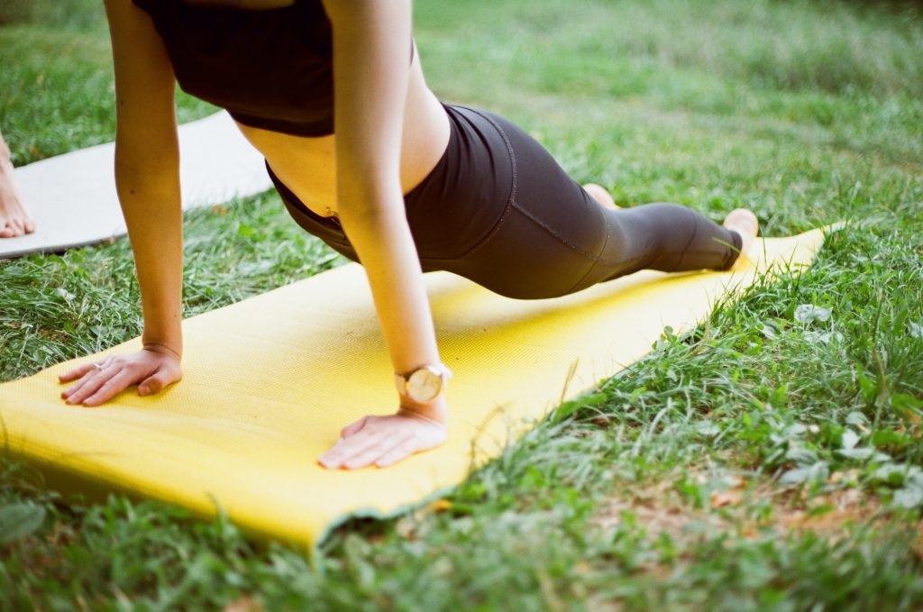 Female person doing a yoga stretch on a yellow mat outdoors, on top of grass